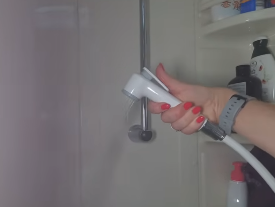Mano che impugna un doccino bianco con pulsante all'interno della doccia del camper
