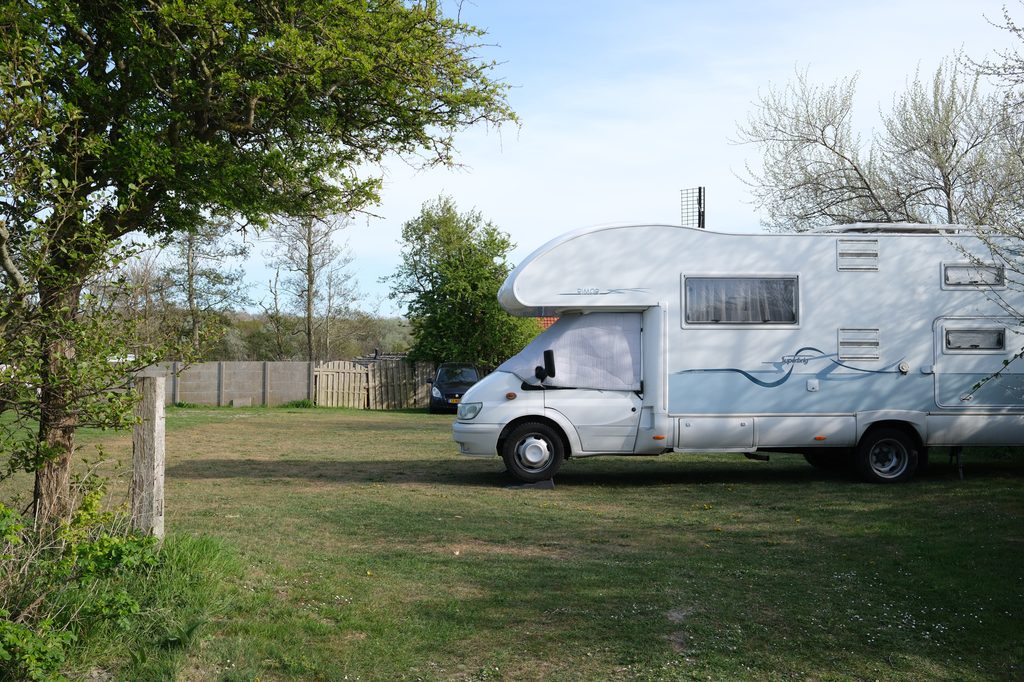 Camper mansardato bianco parcheggiato su un prato, circondato da alberi e vegetazione