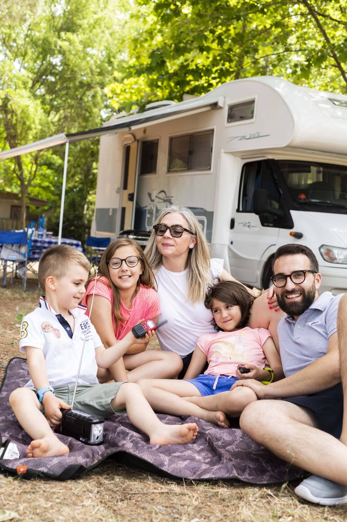 Famiglia di cinque persone seduta insieme su una coperta davanti al camper durante una sosta